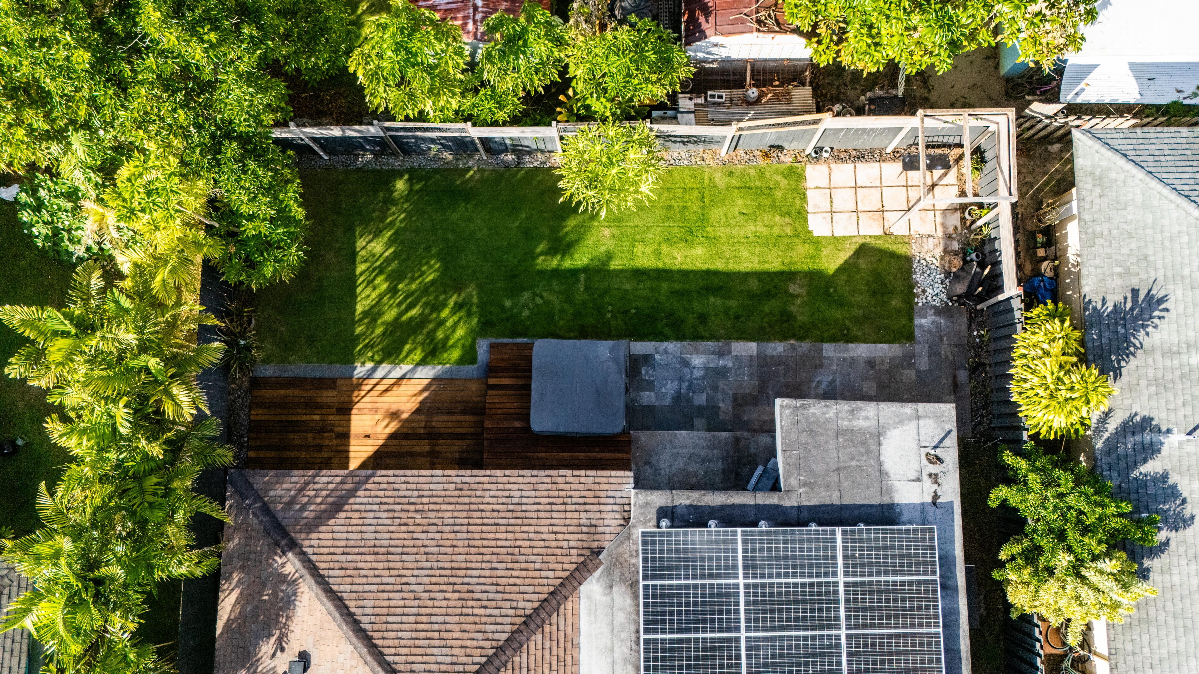 Overhead aerial view of the backyard showing the wood deck, hot tub, solar panels, and lush lawn