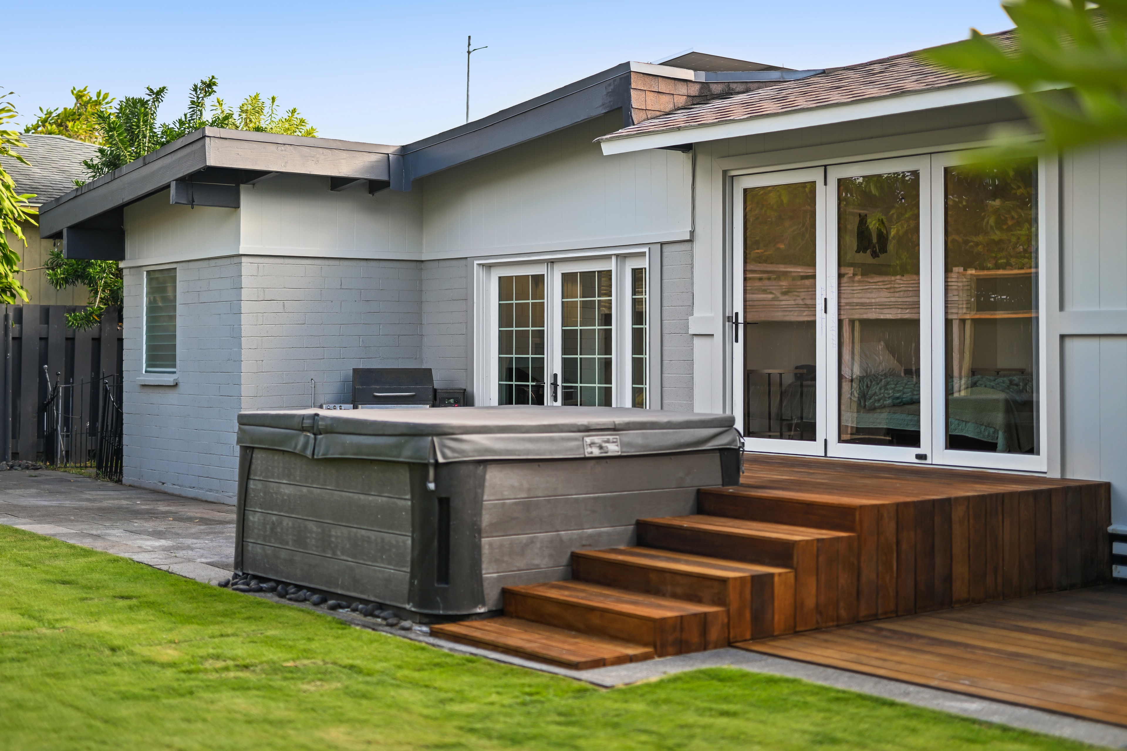 Backyard in daylight — hot tub with cover, wood deck stairs, French doors, and lush lawn