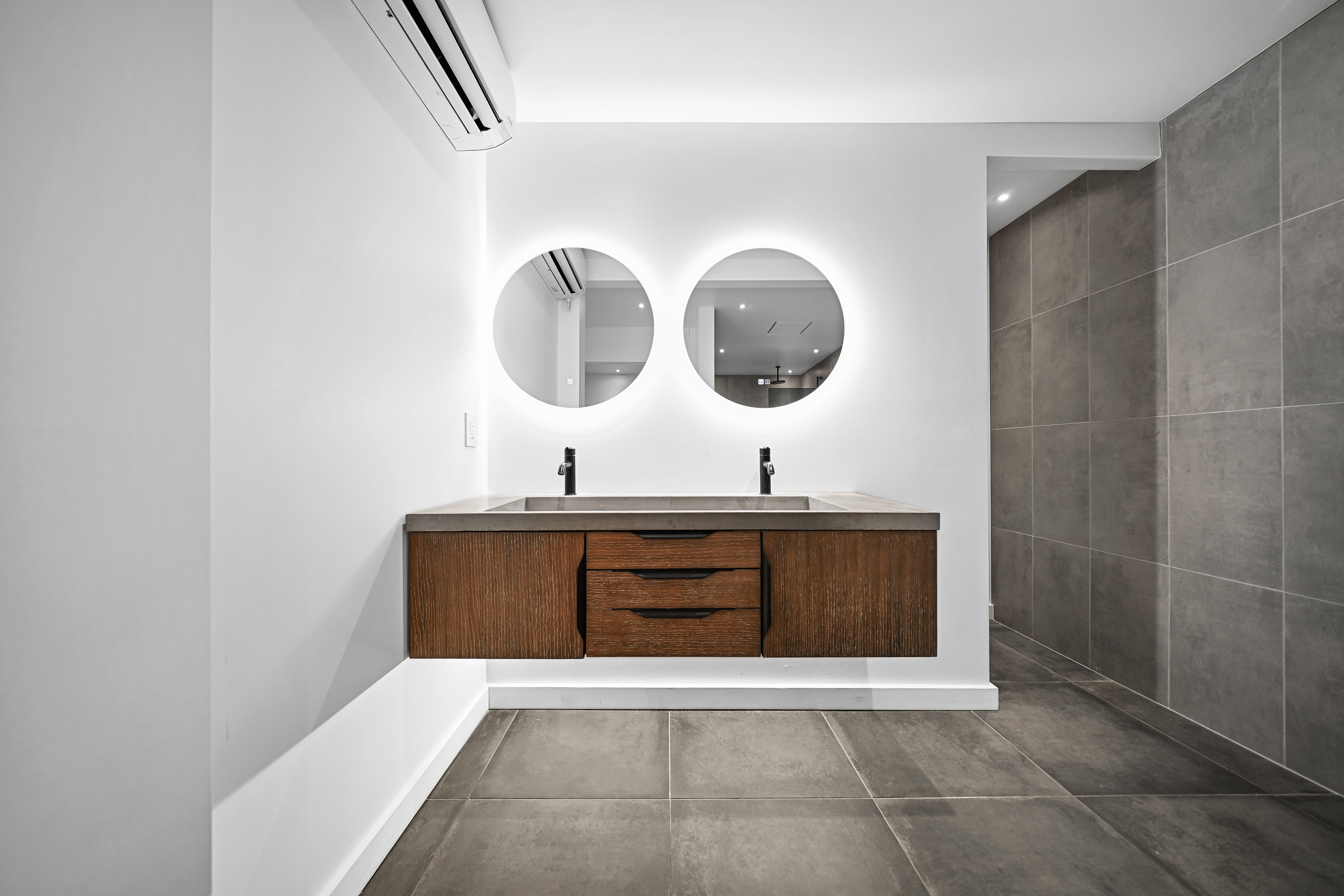 Primary bath with dual concrete sinks, backlit round mirrors, and large-format tile