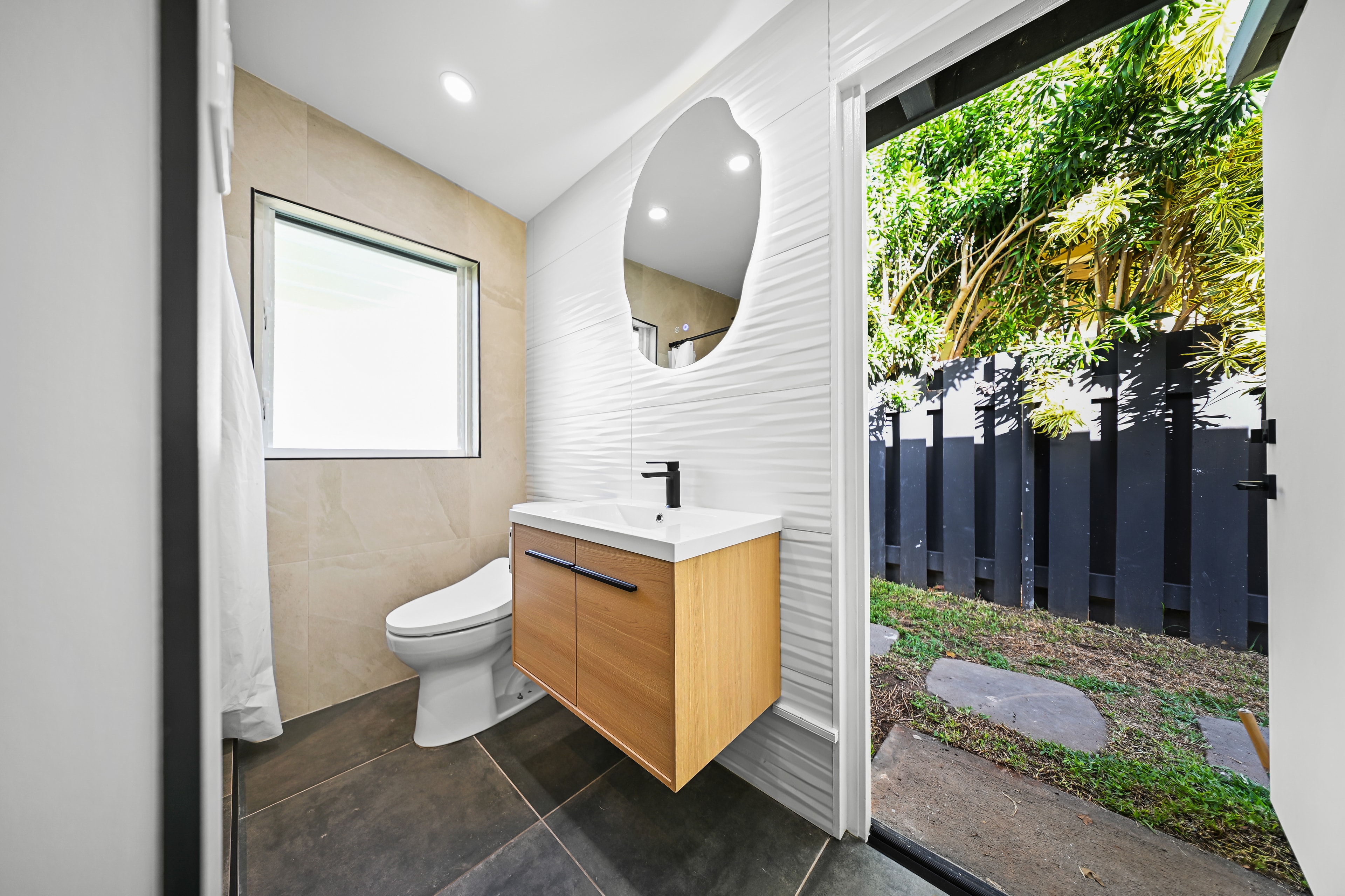 Secondary bathroom with wood vanity, sculptural mirror, and garden access