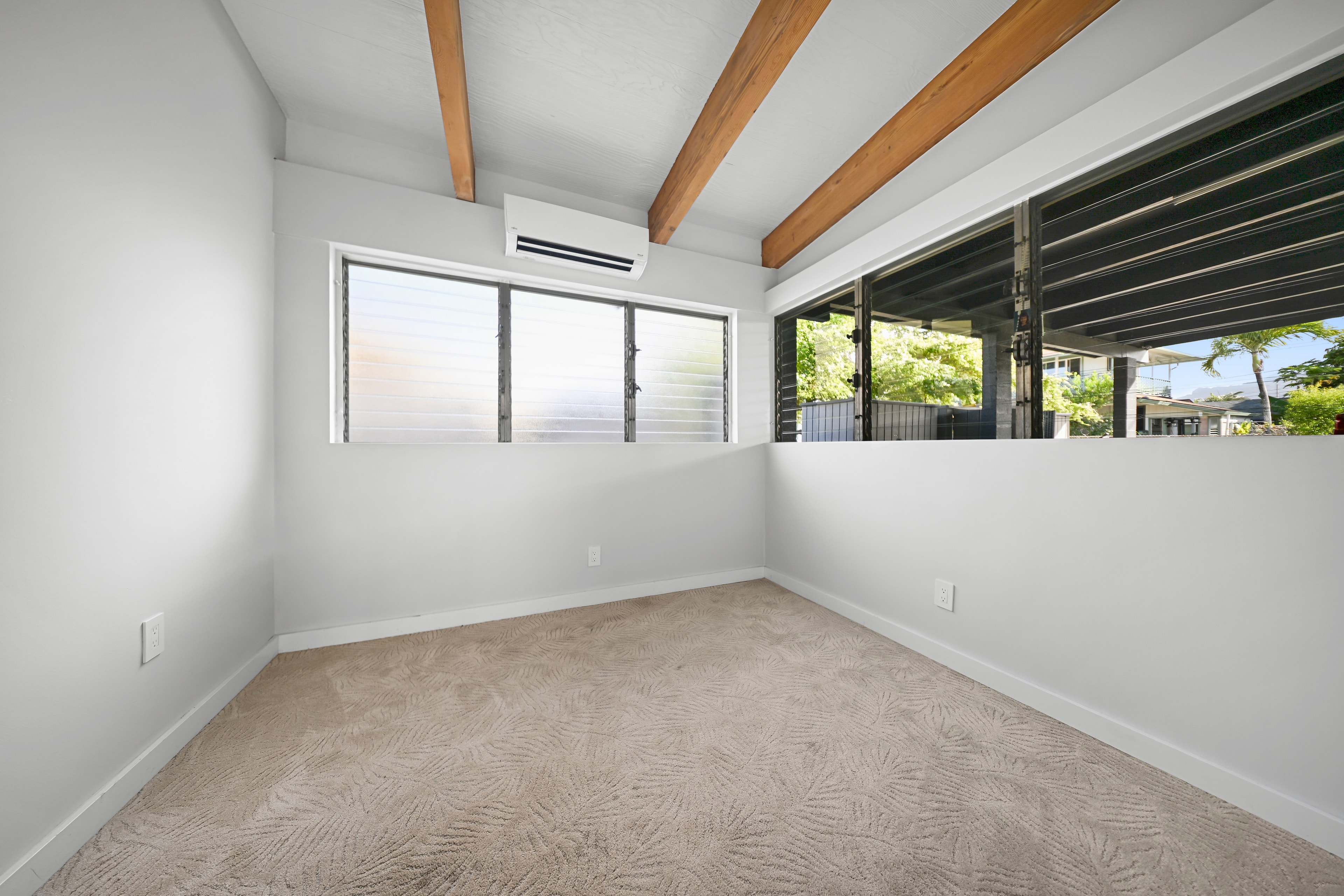 Bright bedroom with exposed wood beams, louvered windows, and mini-split AC