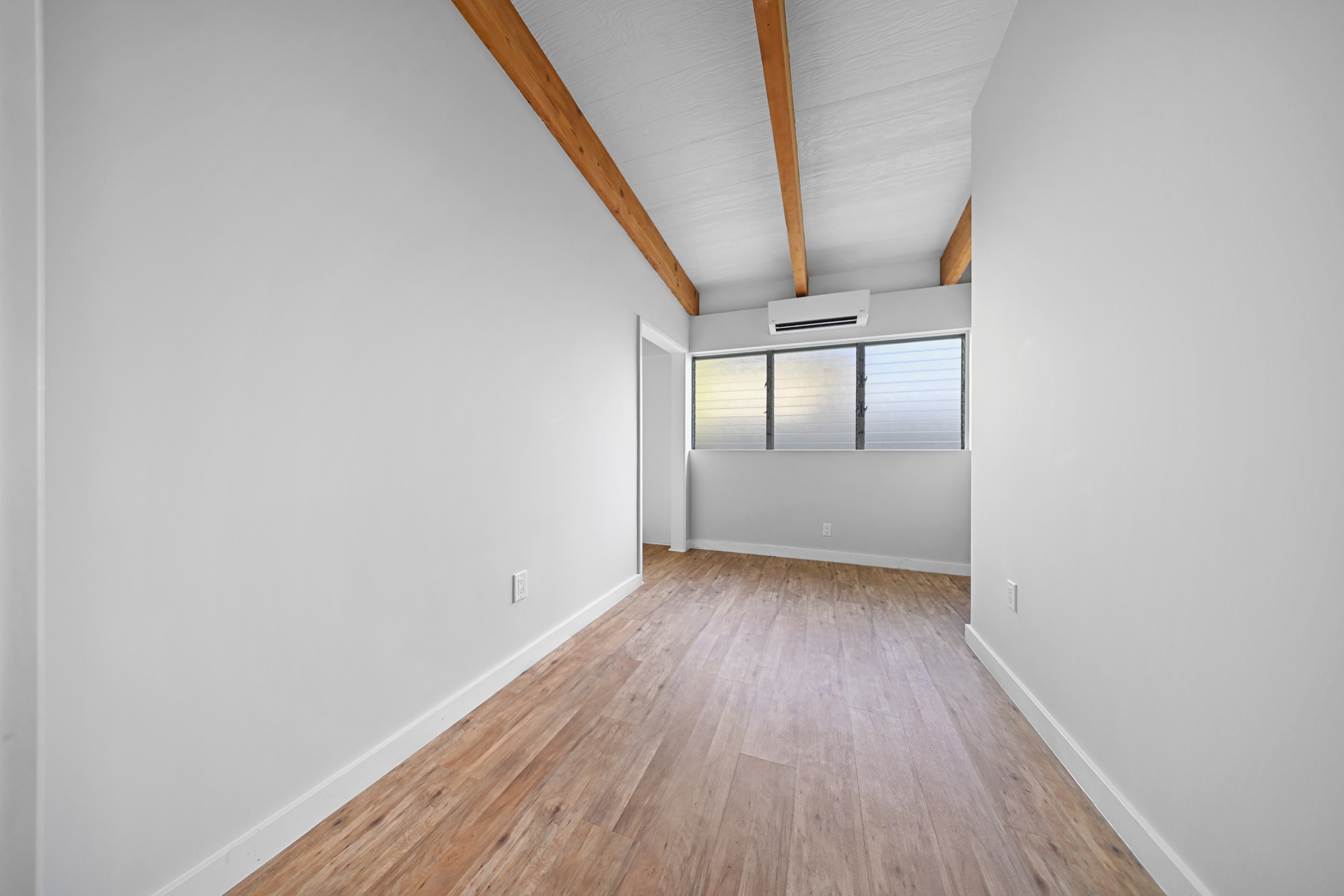 Airy bedroom with vaulted ceiling, wood beams, and louvered windows