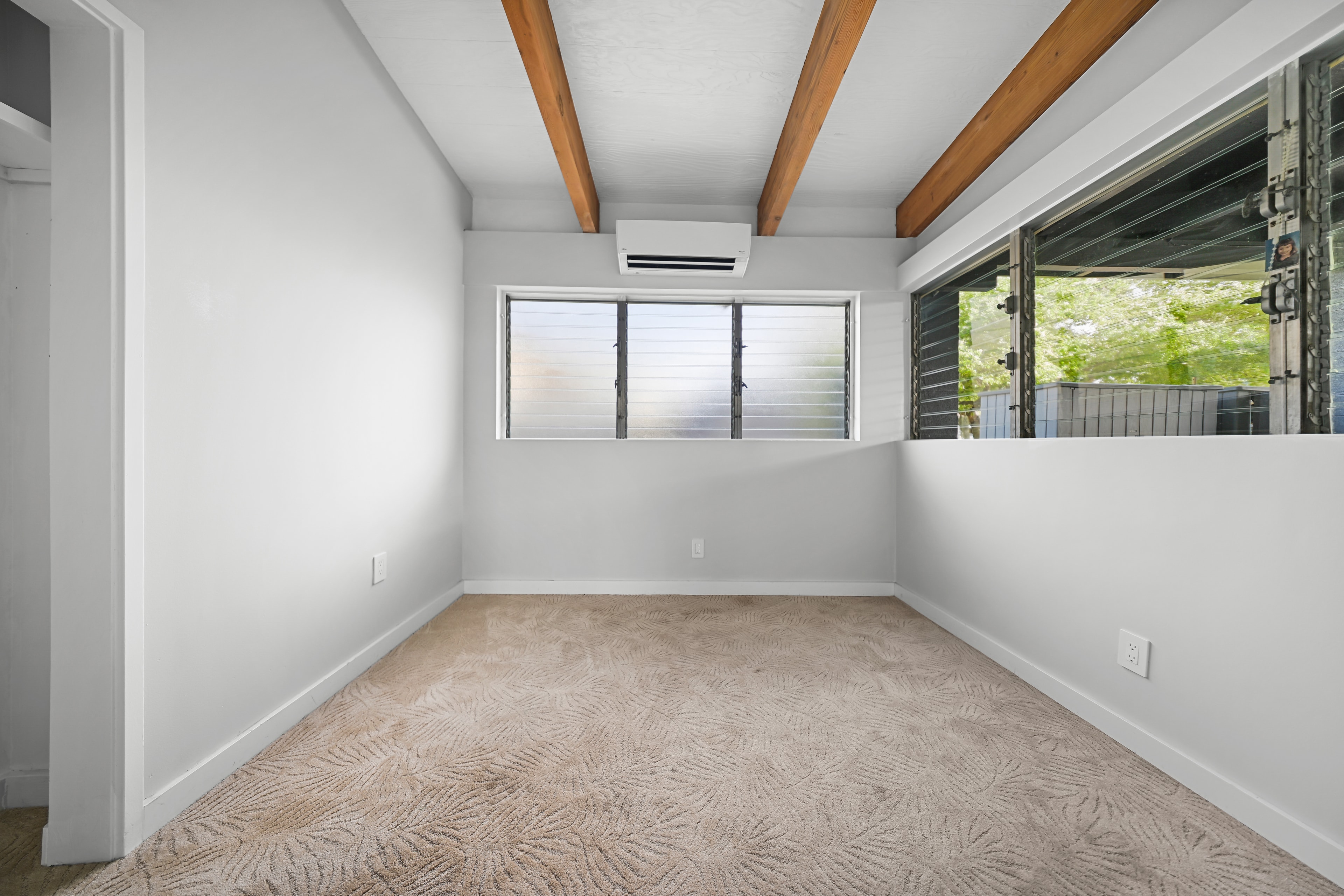 Bedroom with patterned carpet, wood beams, louvered windows, and mini-split AC