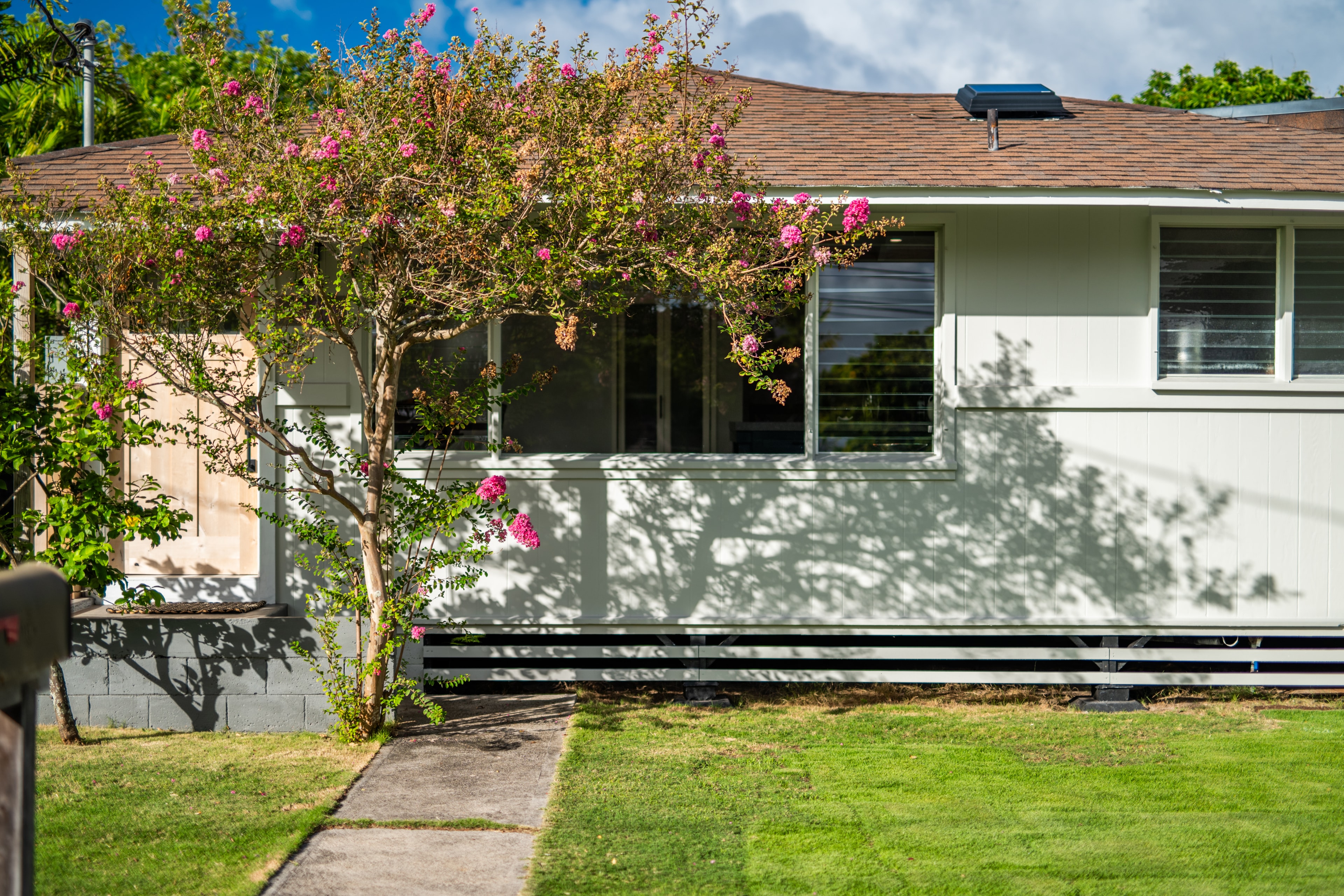 Front exterior with blooming crape myrtle tree, pink flowers, and lush green lawn