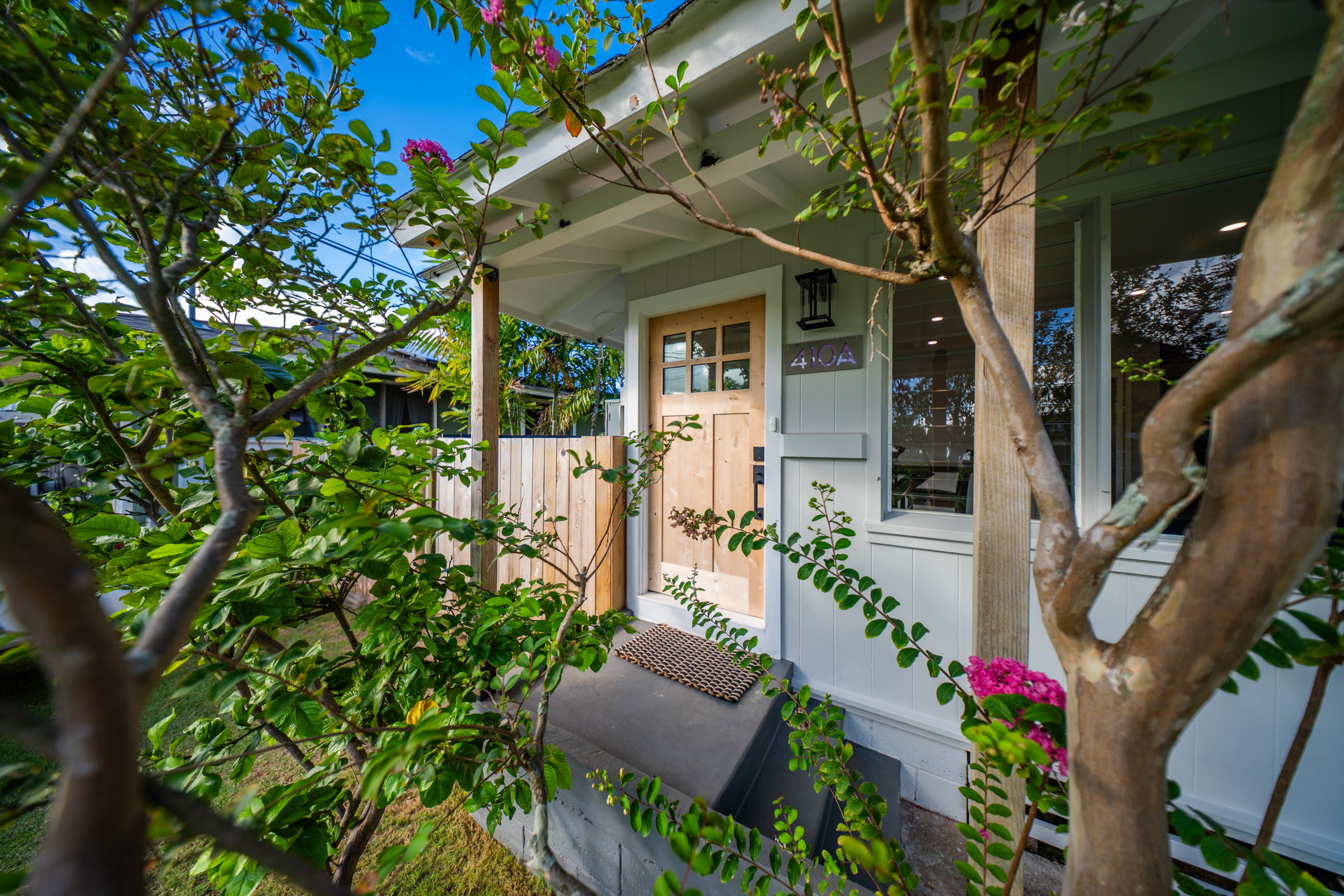 Front entry framed by lush garden — natural wood door, 410A sign, and bougainvillea