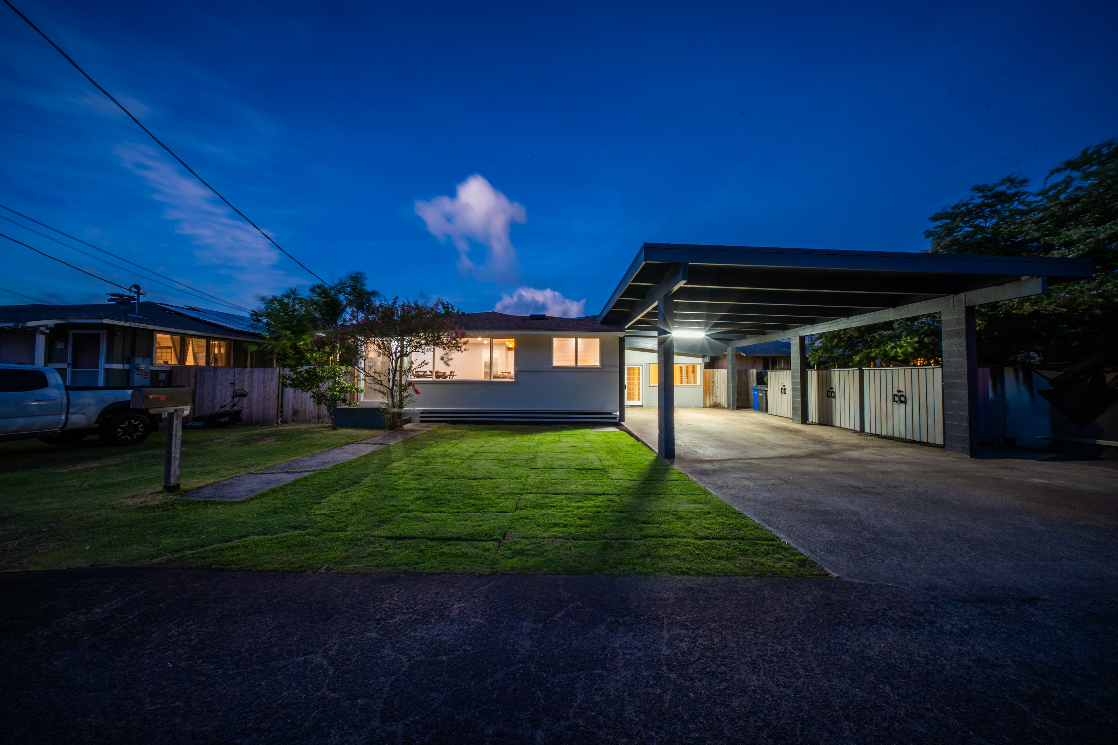 Wide night shot showing front lawn, carport, and full exterior