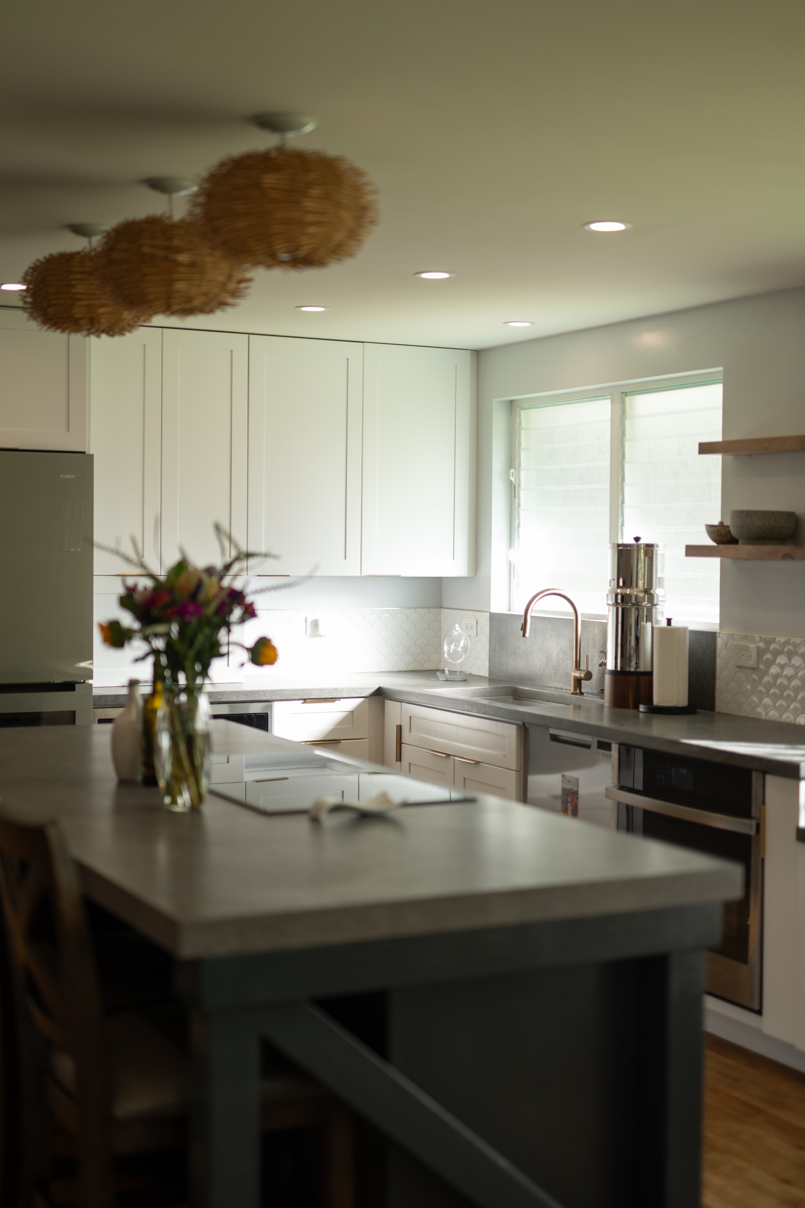 Chef's kitchen with concrete island, white cabinetry, and woven pendant lights