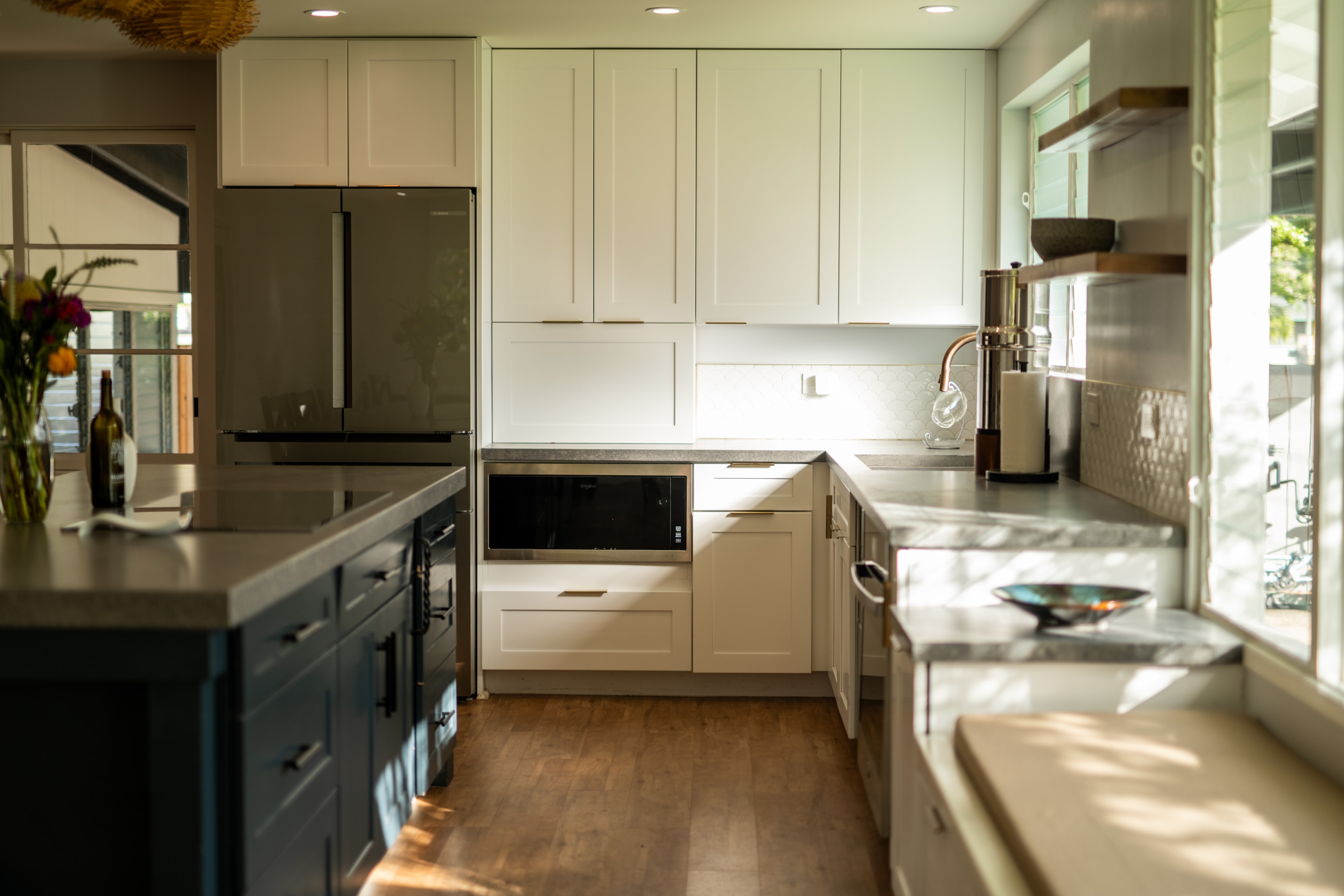 Kitchen showing full wall of white shaker cabinets, dark island, hardwood floors, and woven pendants
