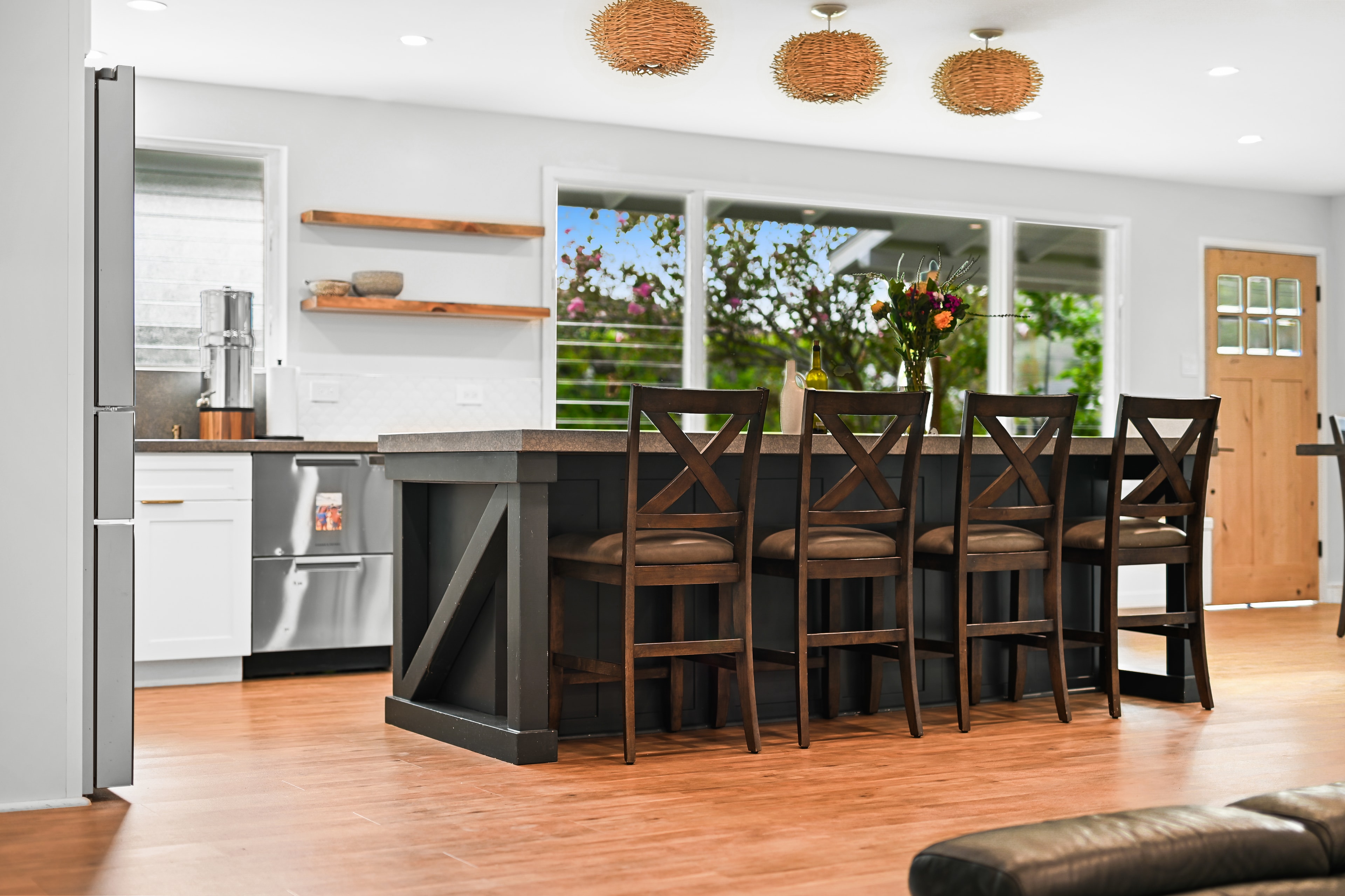 Kitchen island with four bar stools, woven pendant lights, open wood shelving, and garden windows