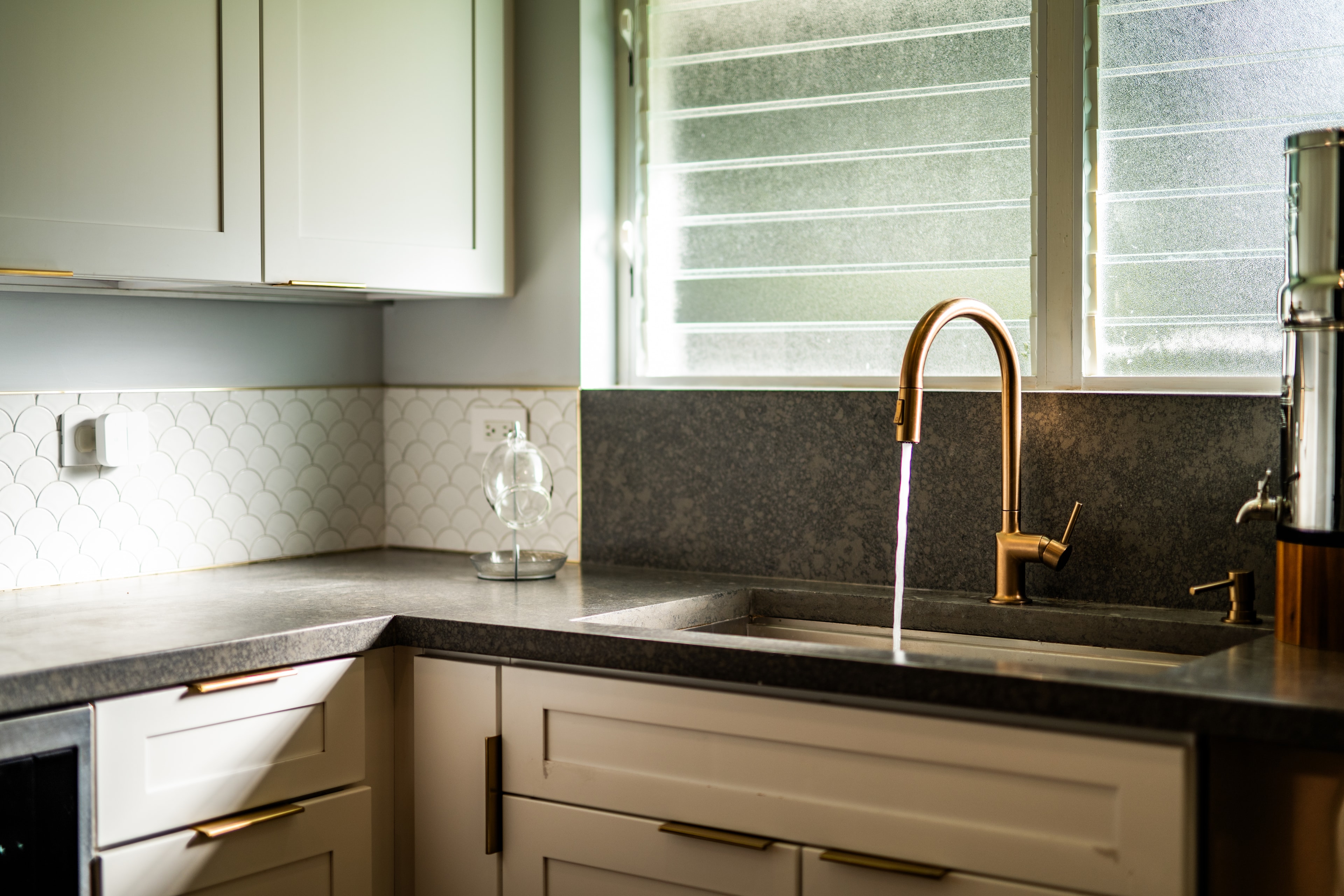 Kitchen sink detail: scallop tile backsplash, concrete counters, and brass gooseneck faucet