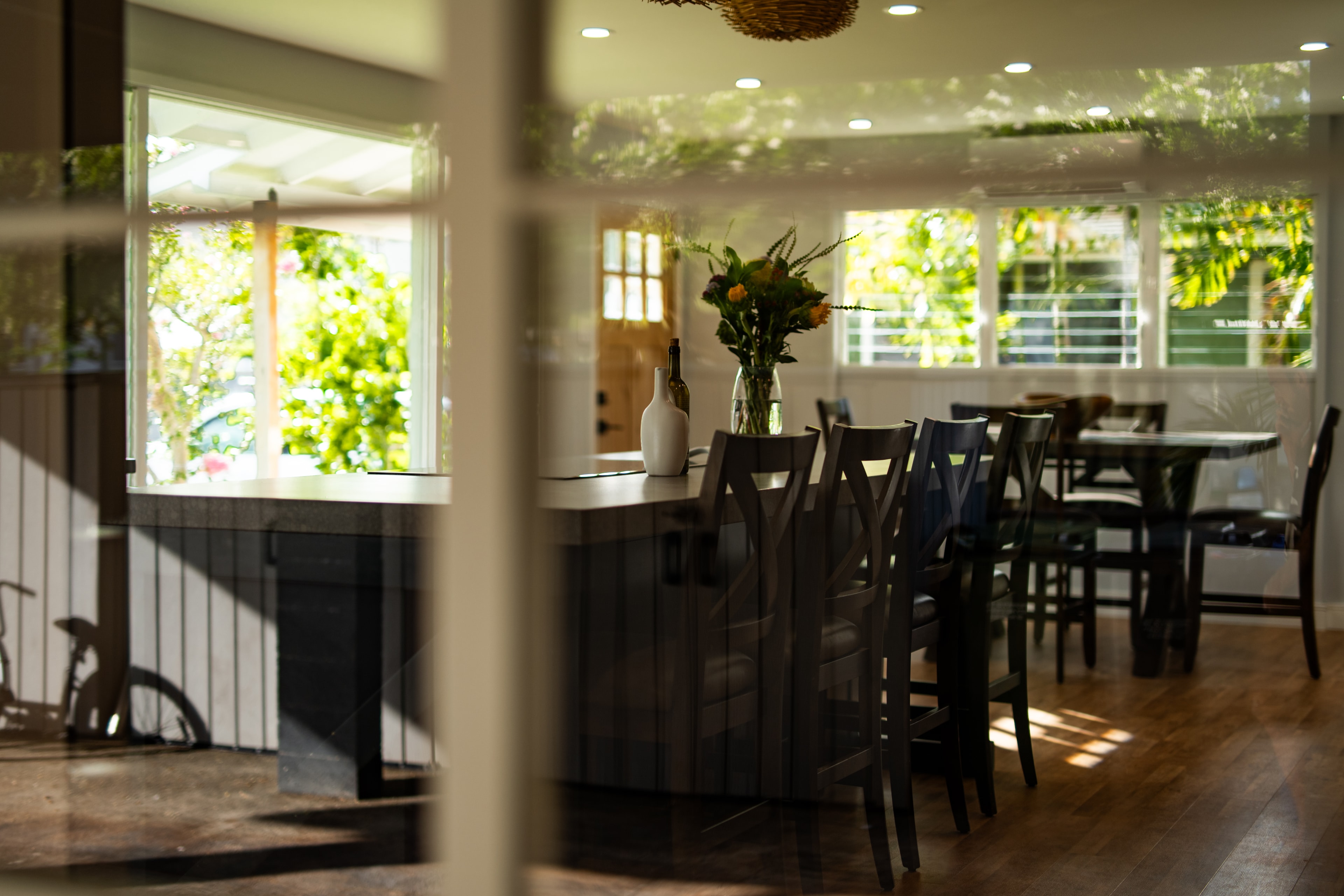 Kitchen island and dining area through the window in bright afternoon light with garden views