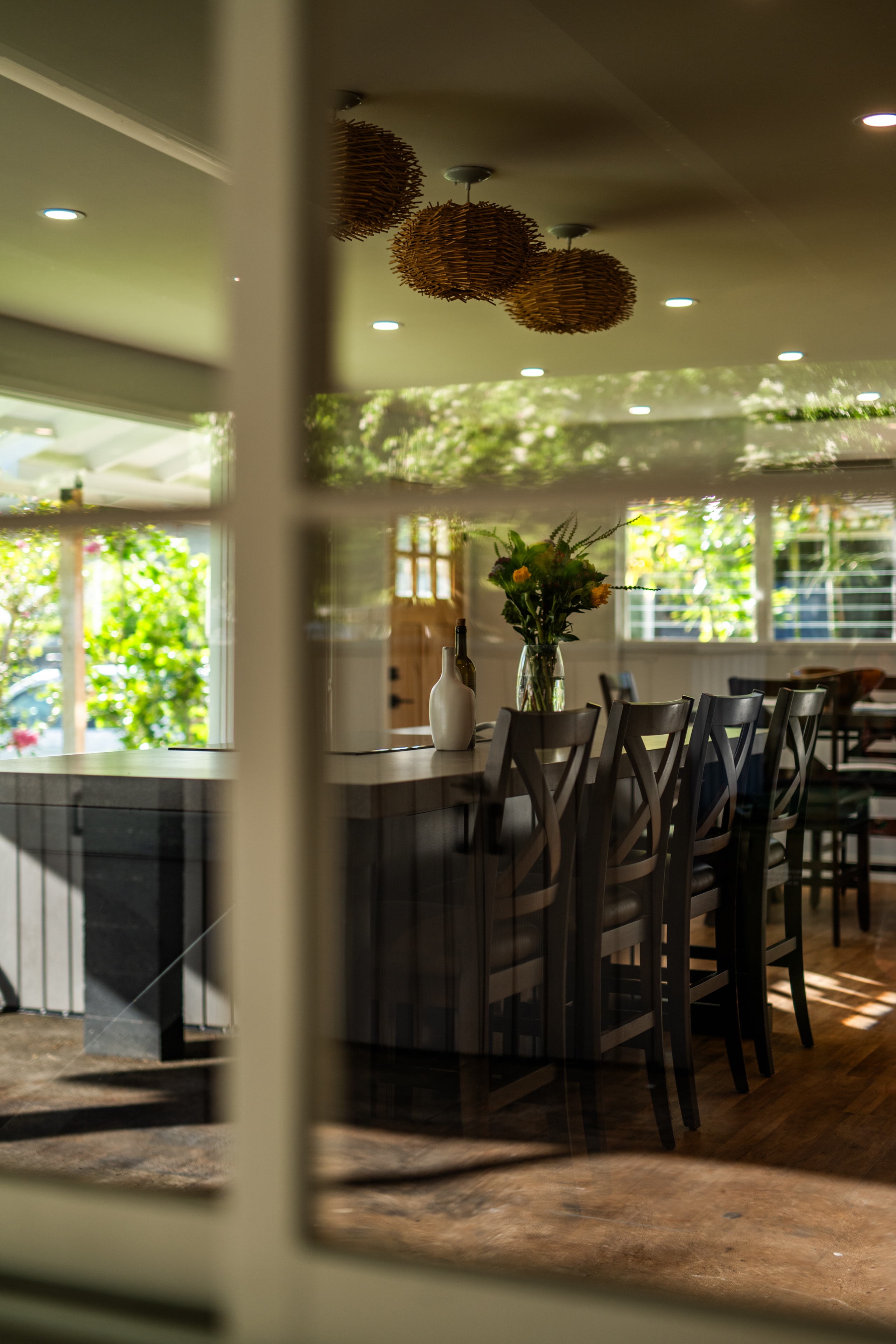 Kitchen and dining area seen through the window — moody natural light, island with fresh flowers