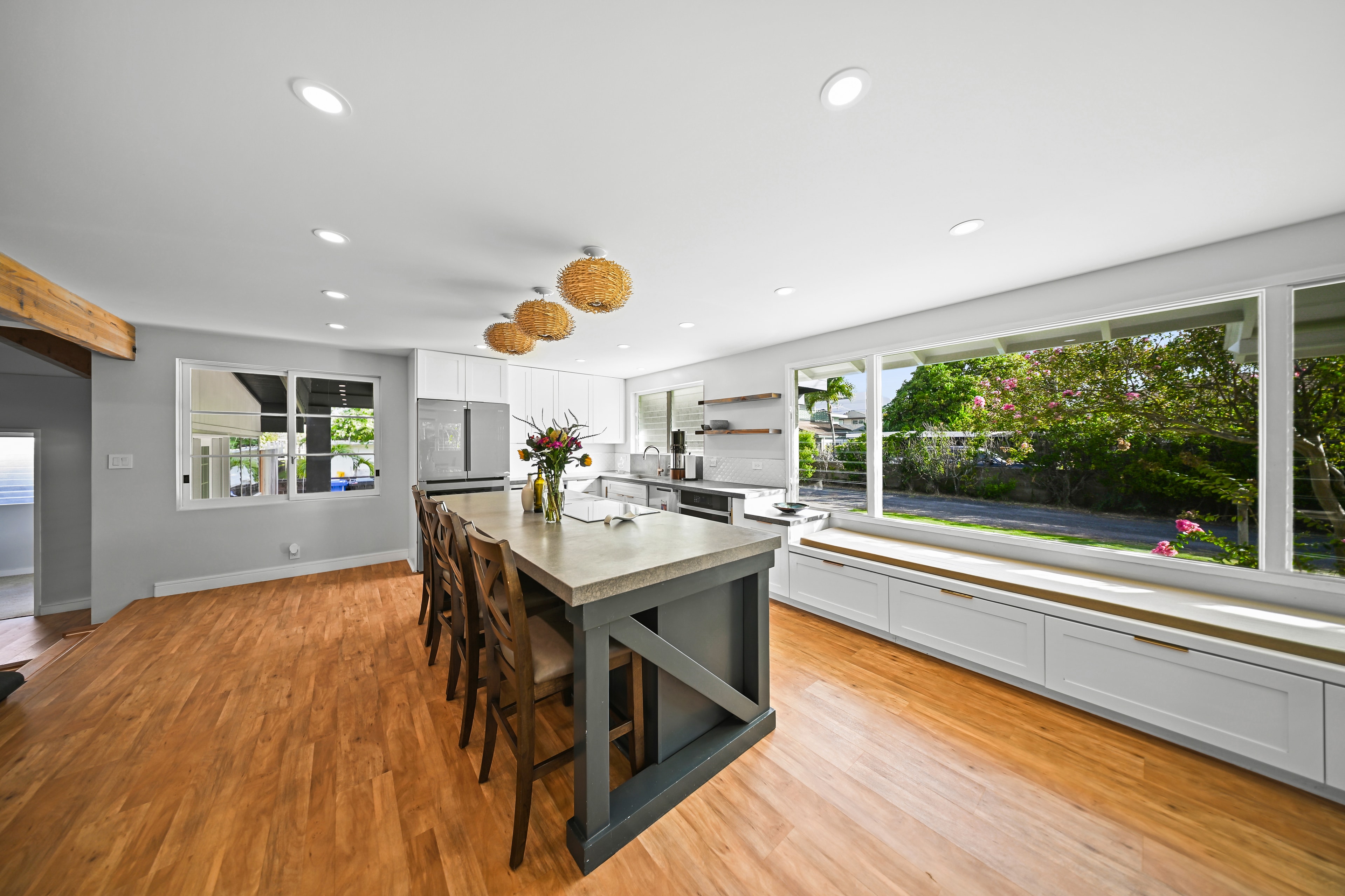 Bright kitchen with large picture windows overlooking the garden, concrete island, and woven pendants