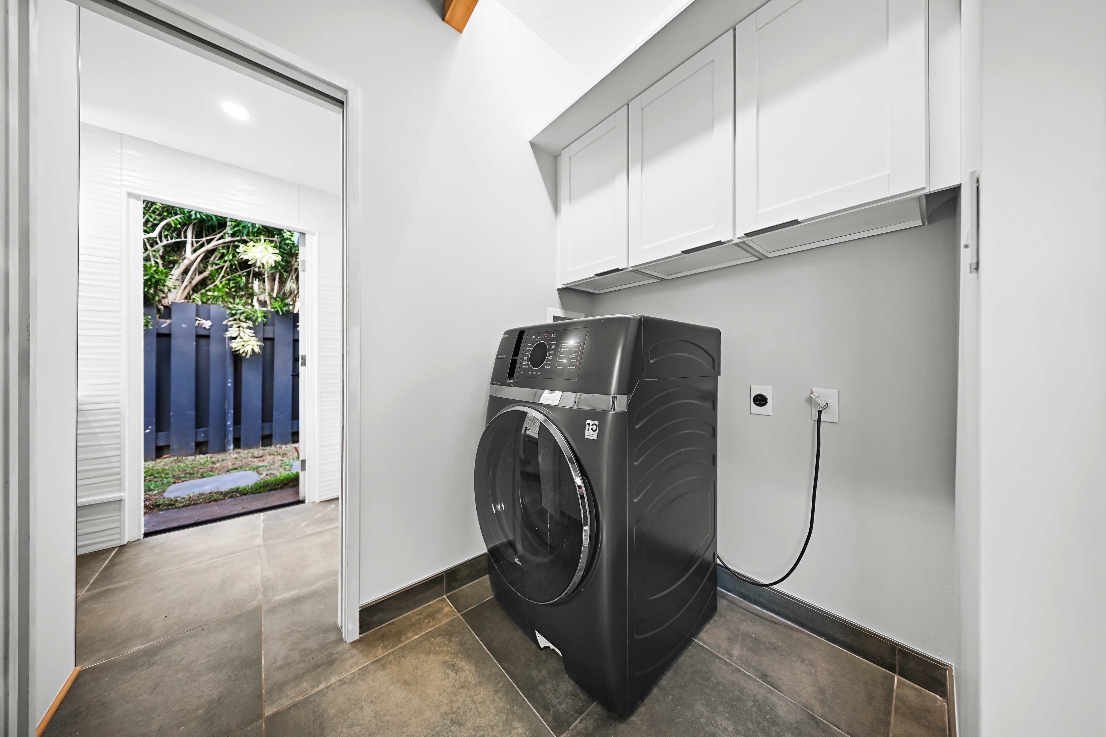 Dedicated laundry room with front-load washer, white upper cabinets, and sliding door to the garden