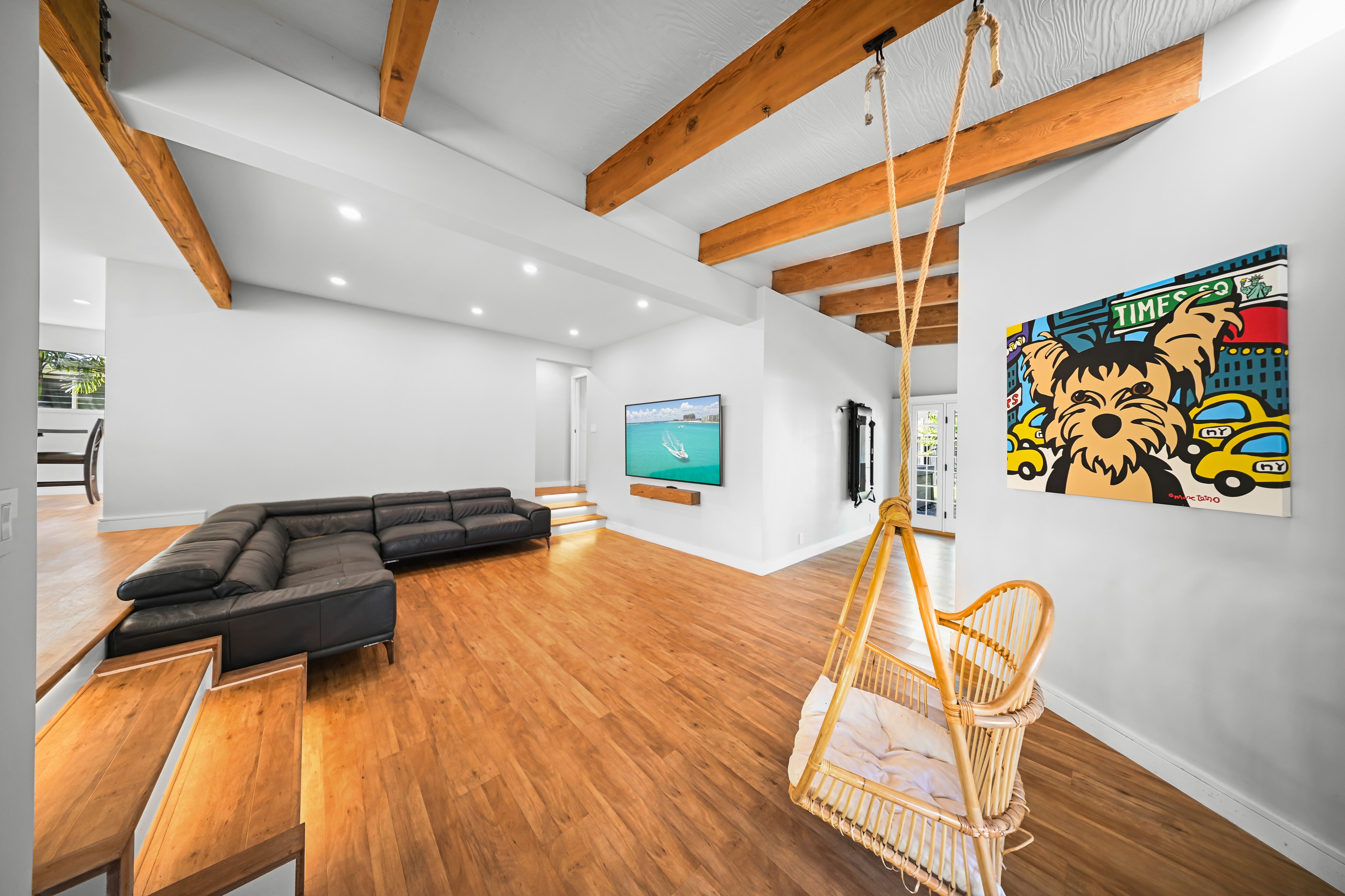 Open living room with exposed wood beams, hardwood floors, and hanging swing chair