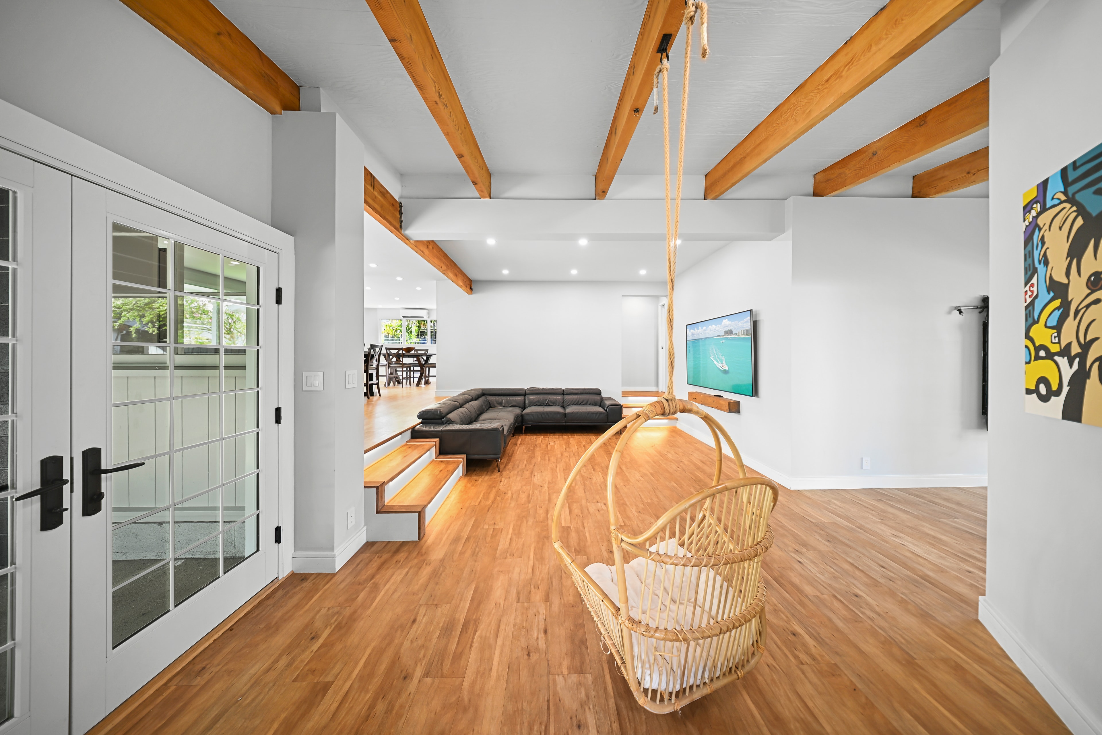 Living room from the entry: rope swing chair, sunken lounge with leather sectional, exposed beams, and TV wall